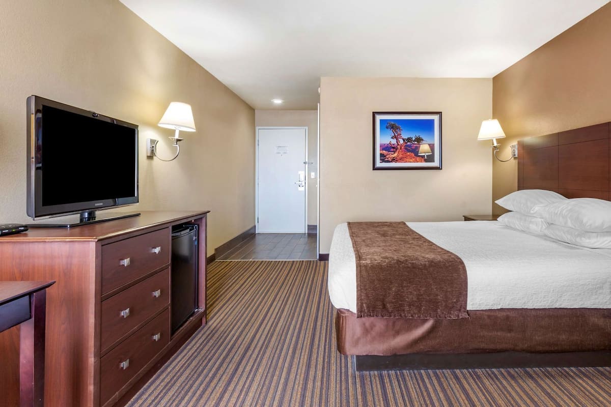 A hotel room with a bed, a TV, a desk with drawers, and a painting on the wall.