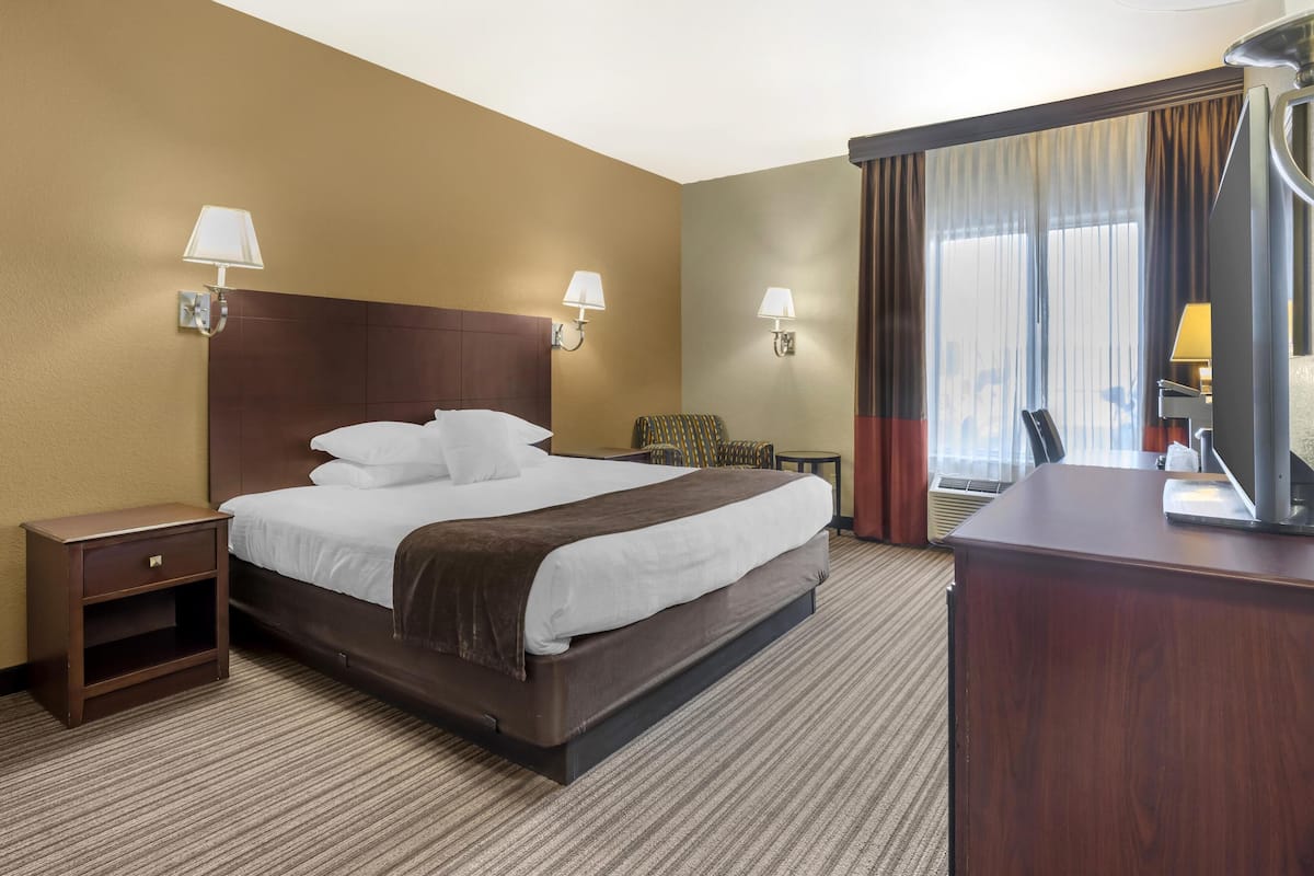 A hotel room with a large bed, two bedside lamps, a nightstand, a desk, and a chair.
