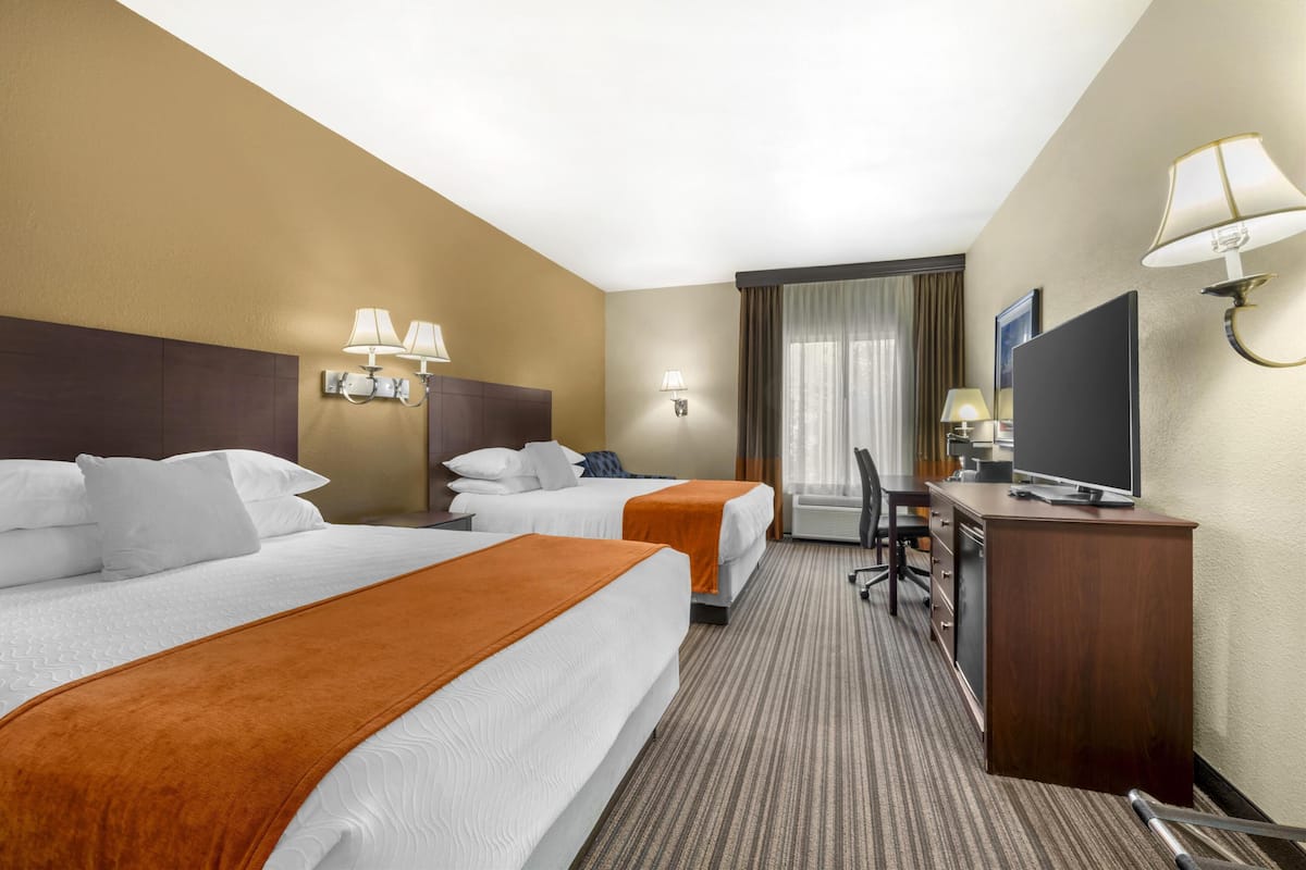 A hotel room with two beds, a desk, a television, and a window with curtains.