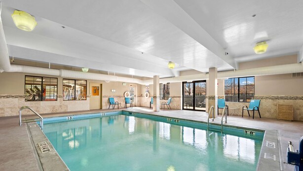An indoor swimming pool with clear water, surrounded by lounge chairs and a view of the outdoors.