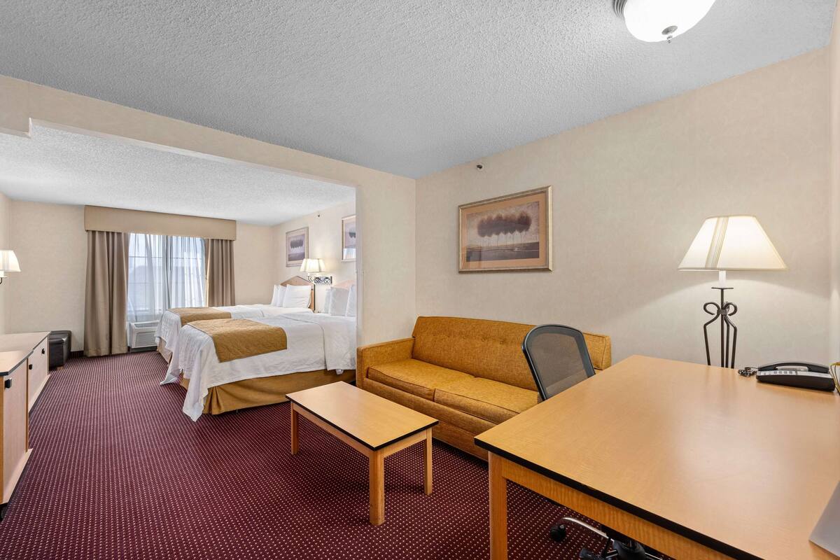 A hotel room with two beds, a sofa, a desk, a chair, and a lamp.