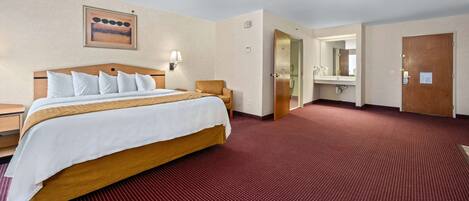 A hotel room with a large bed, a wooden headboard, a red carpet, a wall-mounted lamp, and a door leading to a bathroom.