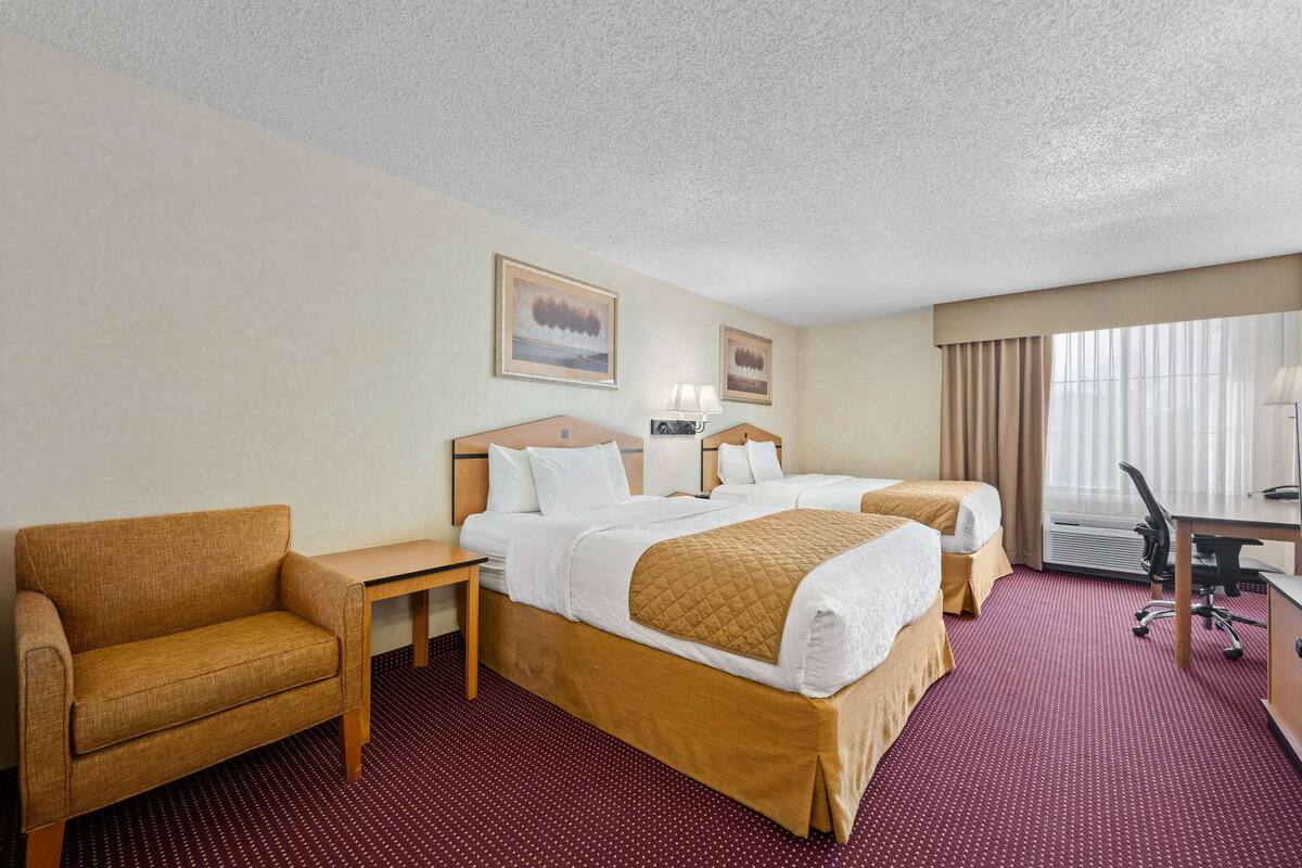 A hotel room with two beds, a sofa, a desk, and a chair.