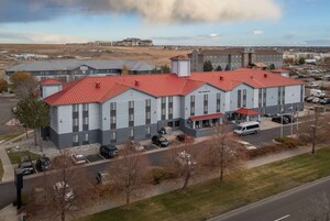 A multi-story hotel with a red roof, parking lot, and surrounding landscape.