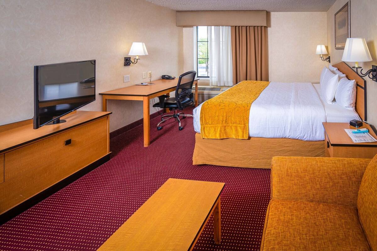 A hotel room with a bed, desk, chair, television, and a window with curtains.