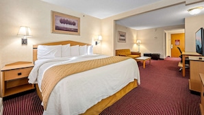 A hotel room with a large bed, a desk, a chair, and a sofa. There are two lamps on the nightstands and a painting on the wall.