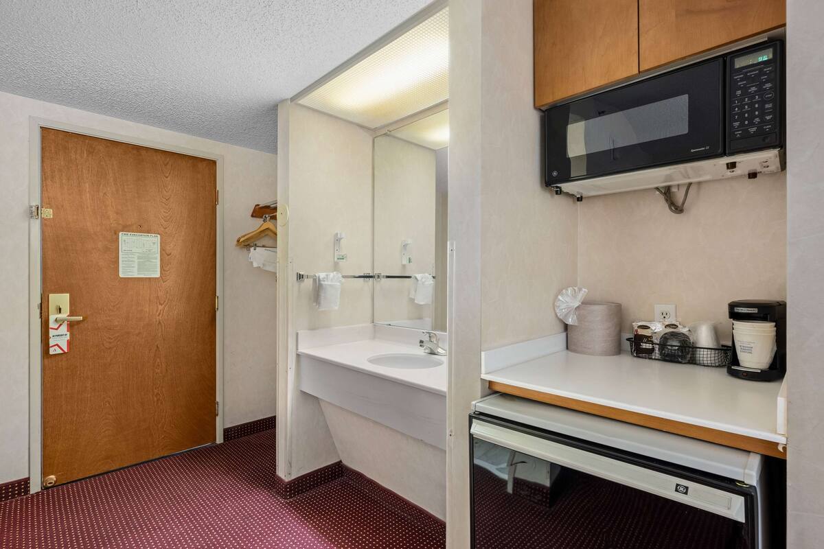 A hotel bathroom with a wooden door, a sink, a mirror, a microwave, and a coffee maker.