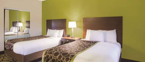 A hotel room with two beds, a nightstand with a lamp, and a mirror.