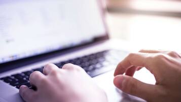 Et nærbillede af hænder, der taster på en bærbar computer.