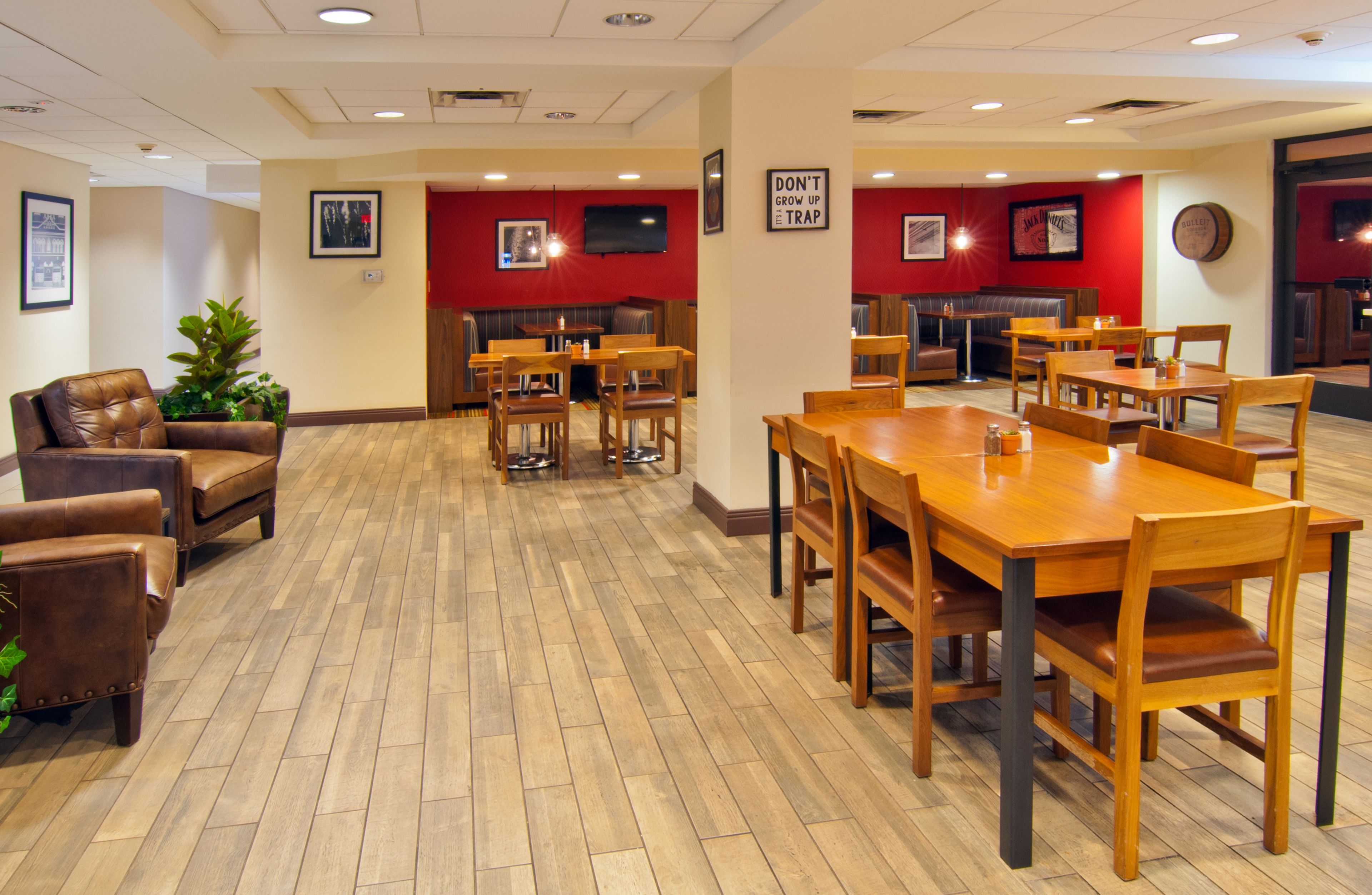 A spacious dining area with wooden tables and chairs, a red accent wall, and a seating area with leather sofas.