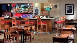Eine Bar mit Holztischen und -stühlen, einer Auswahl an Spirituosen und einem Neonzeichen.