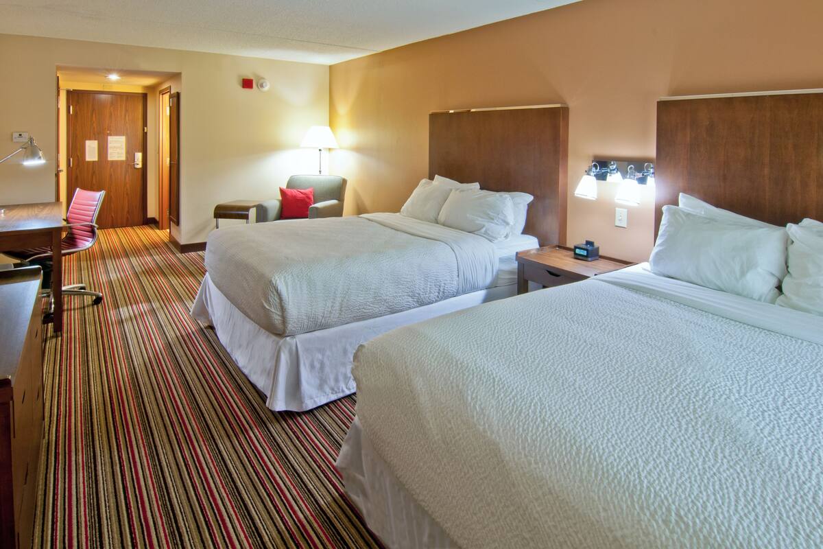 Une chambre d’hôtel avec deux lits, un bureau, une chaise et une lampe.