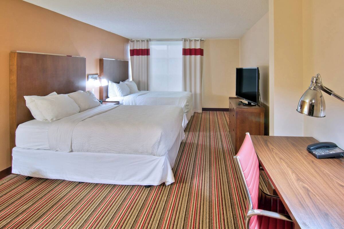 Une chambre d’hôtel avec deux lits, un bureau, une chaise, une télévision et une lampe.