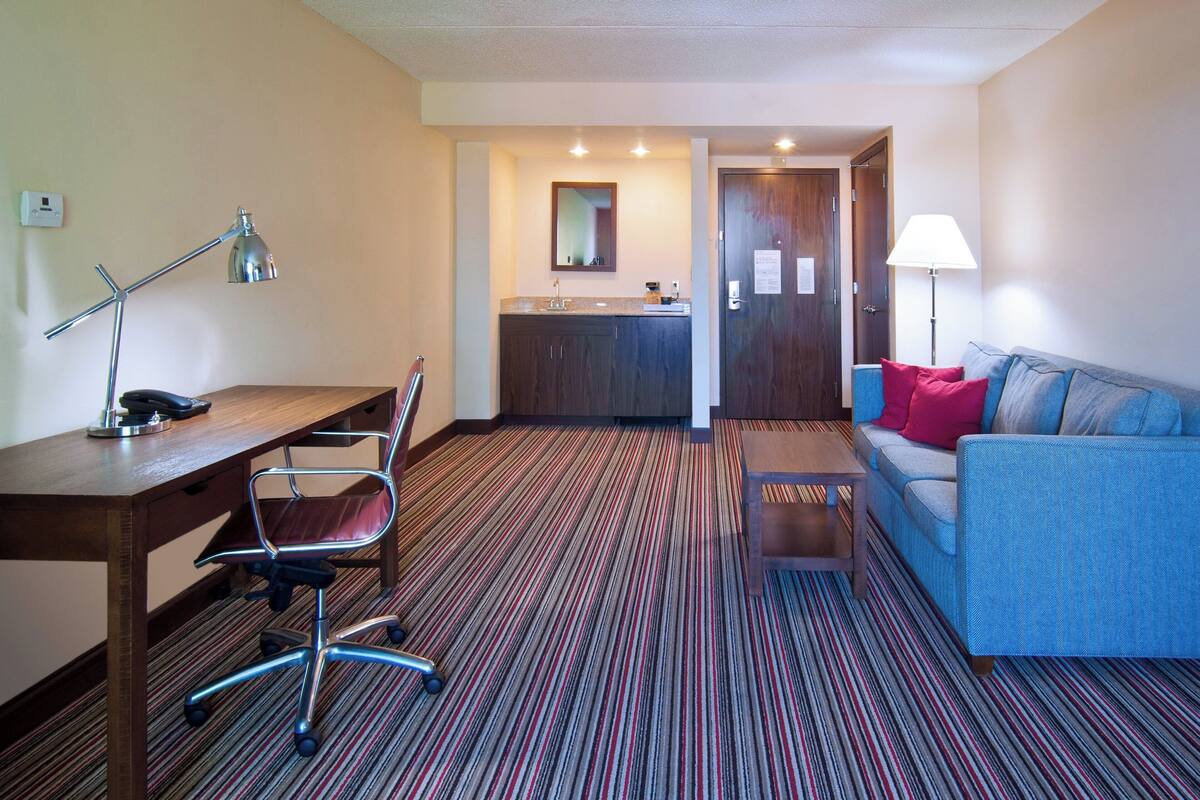 Une chambre d’hôtel équipée d’un bureau, d’une chaise, d’un canapé et d’un petit coin cuisine.