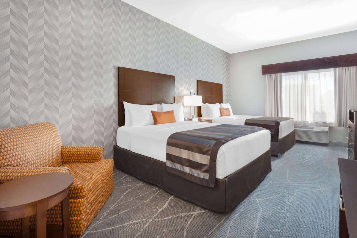 Ein Hotelzimmer mit zwei Betten, einem Schlafsofa, einem kleinen Tisch und einem großen Fenster mit Vorhängen.