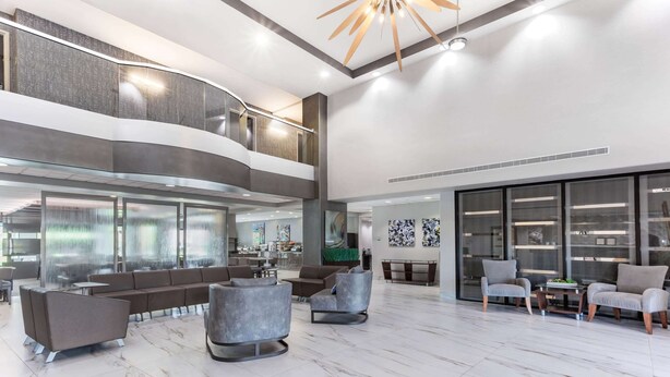 A spacious lobby with a modern design, featuring a seating area with sofas and armchairs, a staircase, and large windows providing natural light. - Wingate by Wyndham Tinley Park (Tinley Park)
