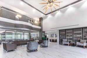 Een ruime lobby met een modern design, met een zithoek met banken en fauteuils, een trap en grote ramen die voor daglicht zorgen.