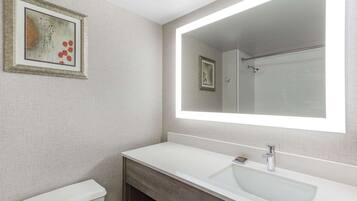 Un baño con un lavabo blanco, un espejo grande y una obra de arte enmarcada en la pared.
