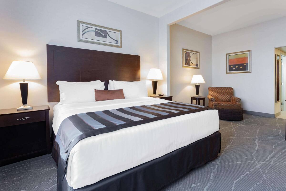 Ein Hotelzimmer mit einem großen Bett, zwei Nachttischen mit Lampen, einem braunen Sessel und Bildern an den Wänden.