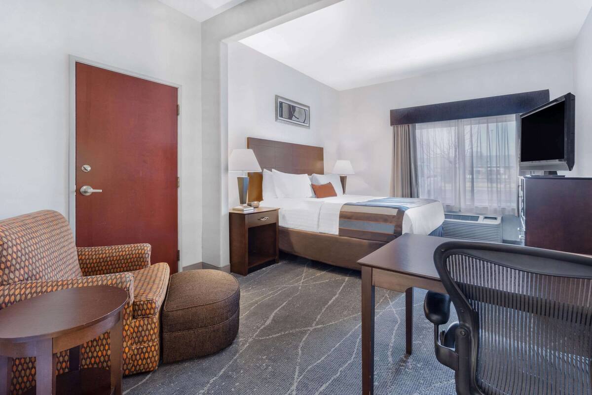 Ein Hotelzimmer mit Bett, Schreibtisch, Sessel, Sofa, Fernseher und einem Fenster mit Vorhängen.