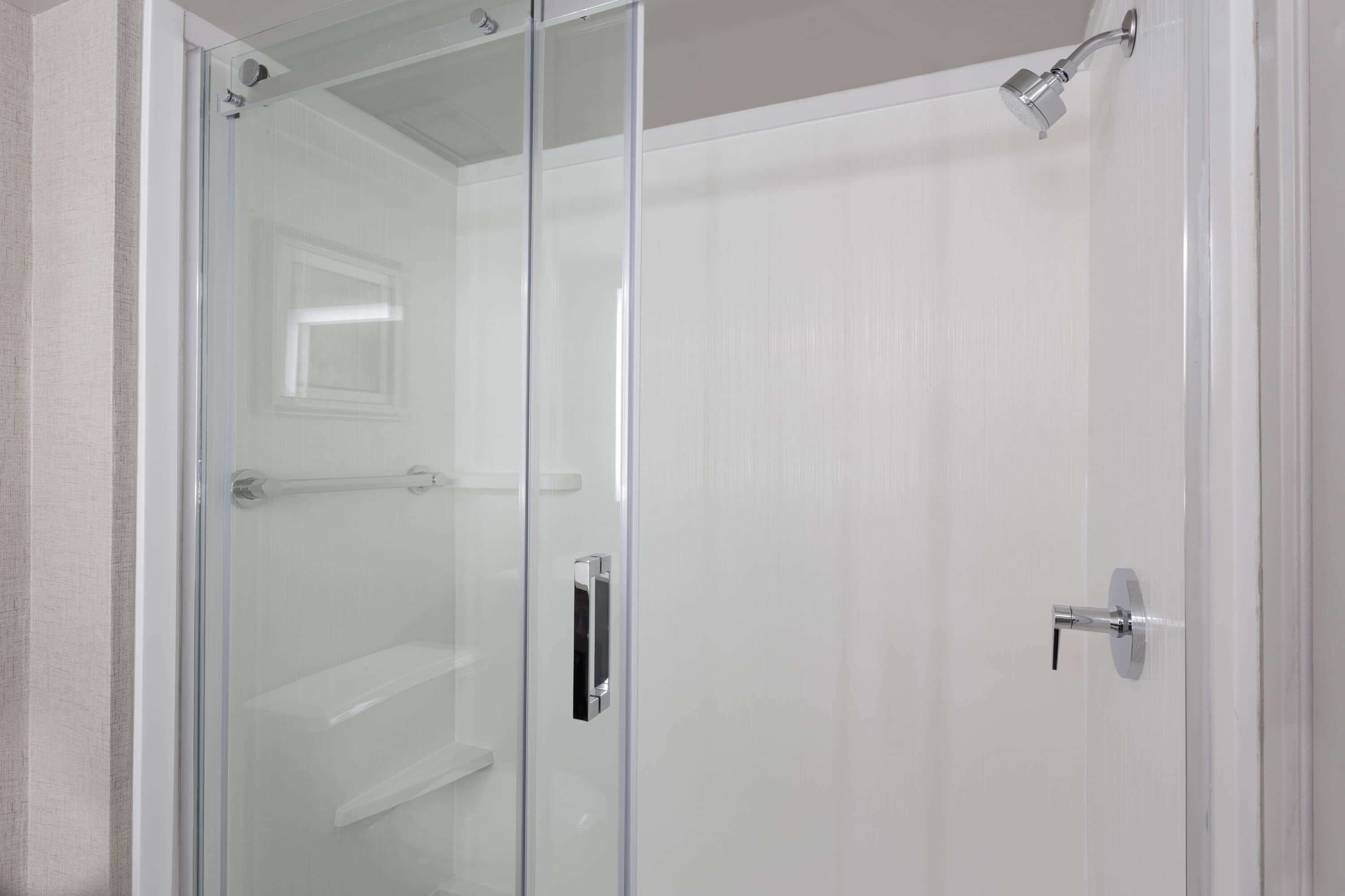 Une douche fermée par des parois de verre, avec une porte blanche et une poignée argentée.