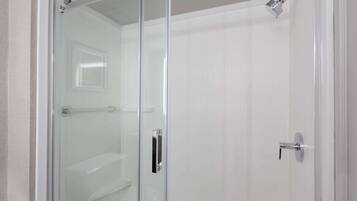 Une douche fermée par des parois de verre, avec une porte blanche et une poignée argentée.