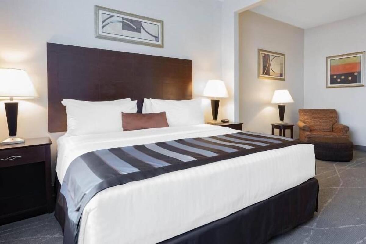 Ein Hotelzimmer mit einem großen Bett, zwei Nachttischen mit Lampen, einem Sessel und Bildern an den Wänden.