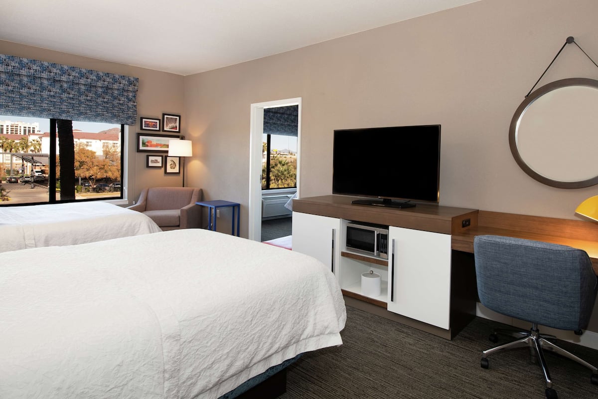 A hotel room with two beds, a desk with a TV, a chair, a lamp, and a view of the outside.