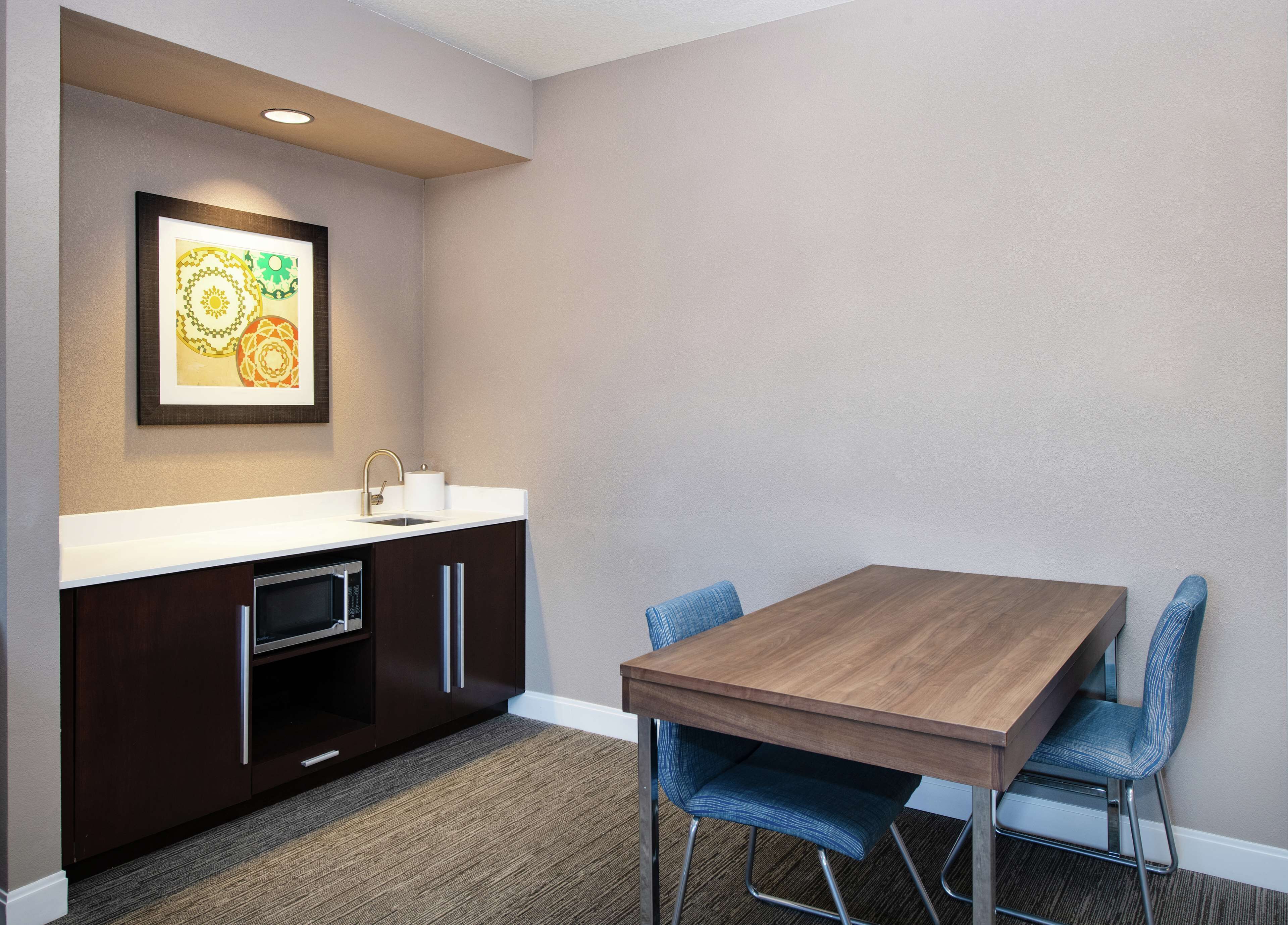 A modern kitchen with a wooden table and blue chairs, a microwave, and a sink.