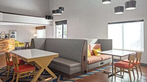 Un moderno vestíbulo de hotel con una zona de estar, una mesa de comedor y un amplio ventanal que proporciona luz natural.