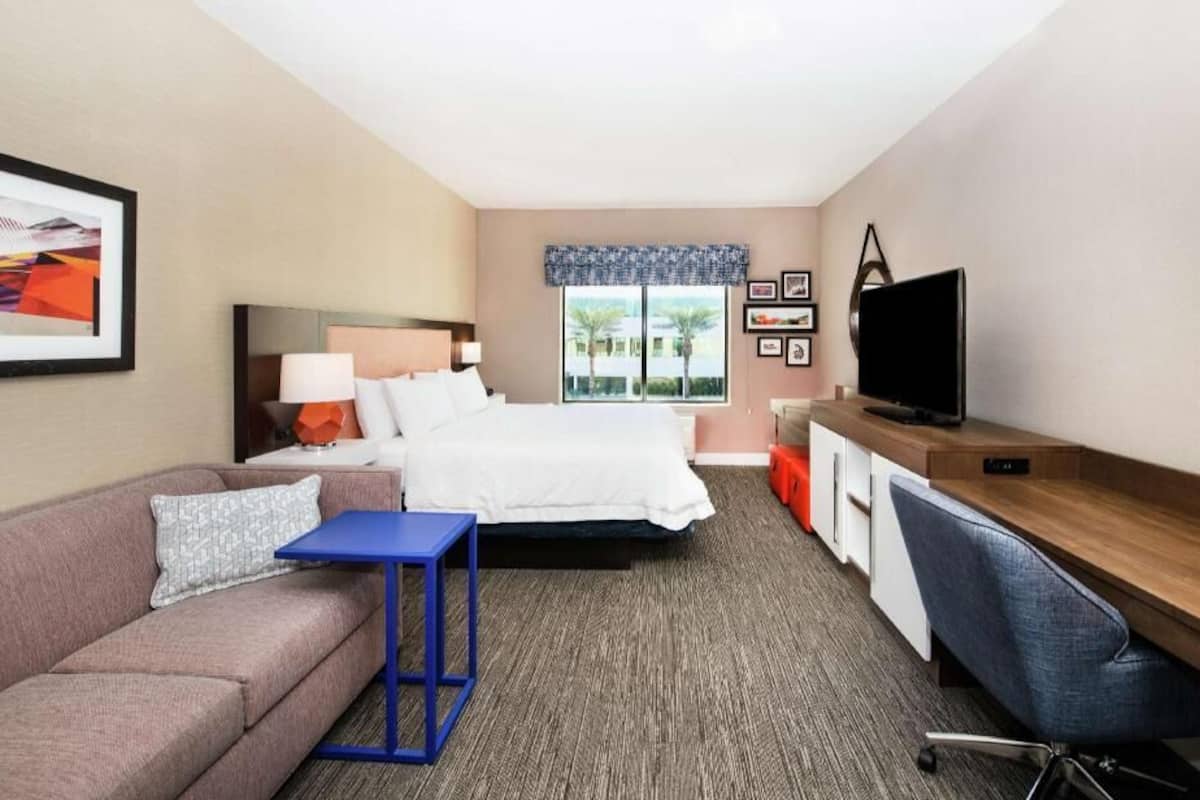 A hotel room with a bed, a desk, a chair, a sofa, a TV, and a window with a view.