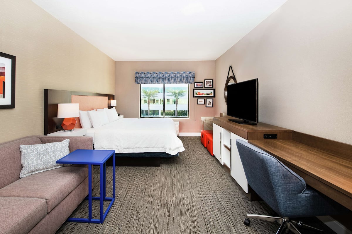 A hotel room with a bed, a desk, a television, and a sofa.