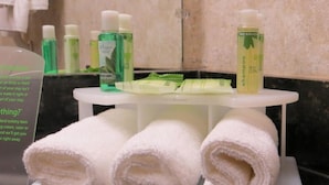 A bathroom with toiletries including a bottle of shampoo, a bottle of mouthwash, and a bottle of lotion. There are three rolled towels on a tray.