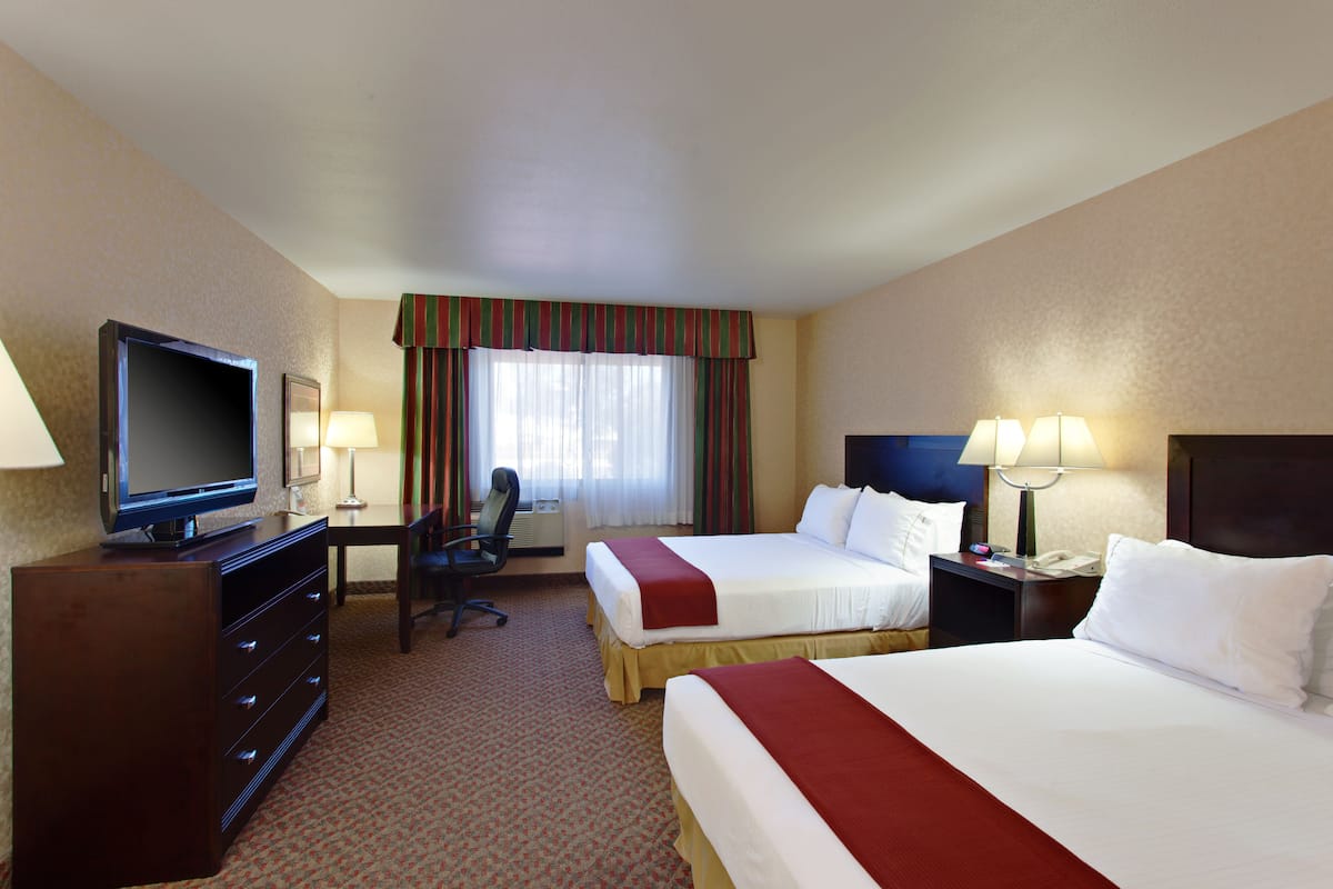 A hotel room with two beds, a television, a desk with a chair, and two bedside lamps.