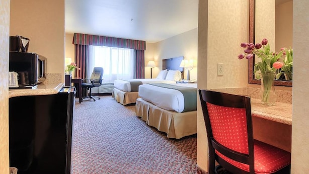 A hotel room with two beds, a desk with a computer, a chair, a mirror, and a vase with flowers.