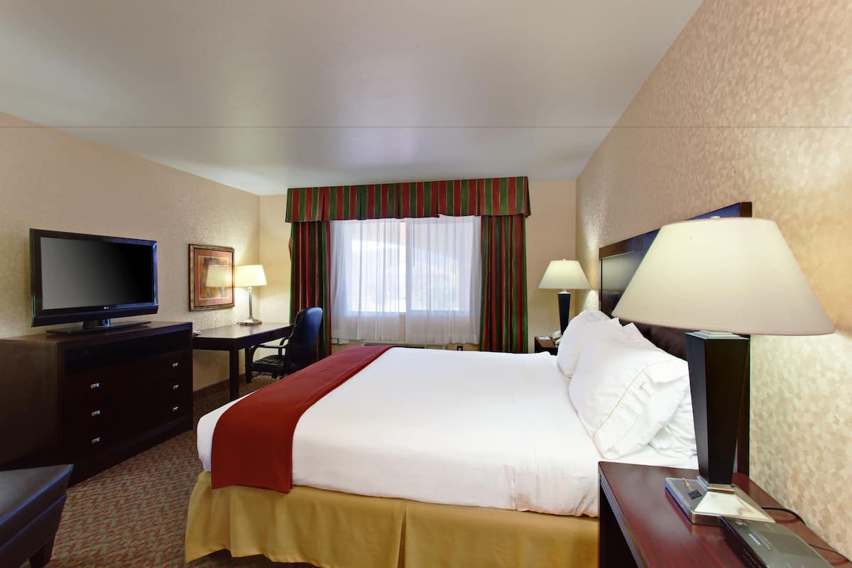 A hotel room with a bed, a desk, a television, and a window with curtains.