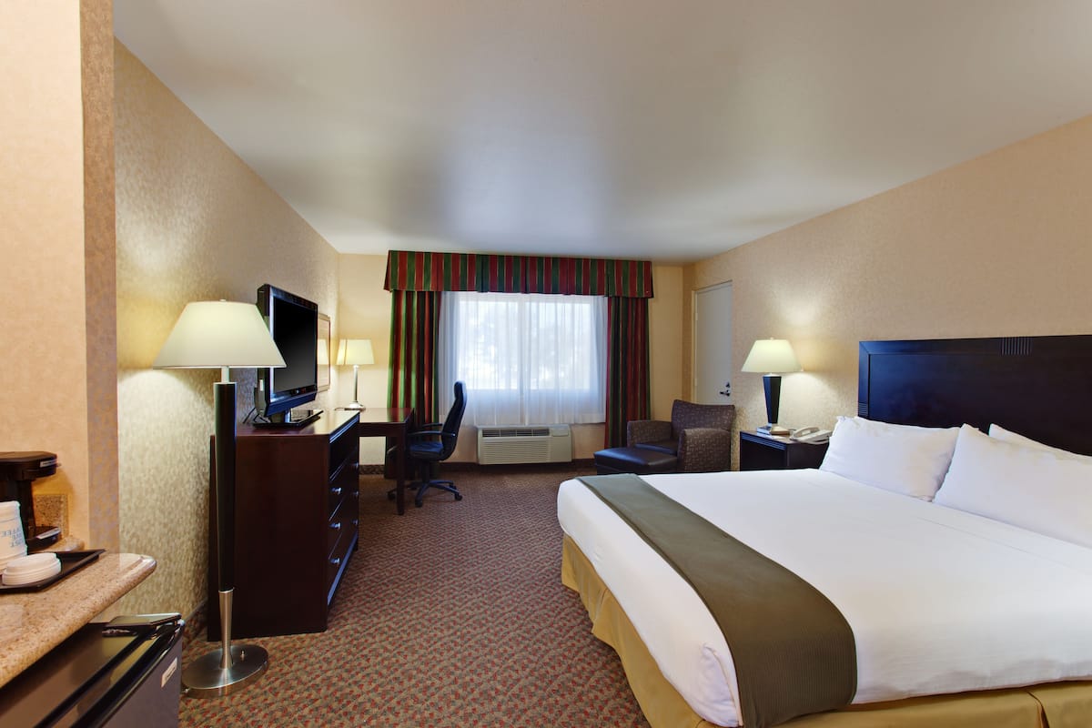 A hotel room with a large bed, a desk with a computer, a TV, and a chair.