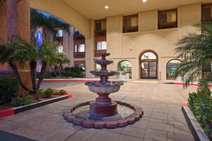 A courtyard with a central fountain, surrounded by palm trees and a building with multiple balconies.