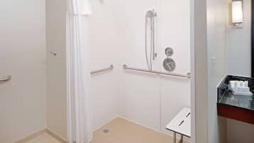 Een badkamer met een douche, handgrepen, een handdoekhouder en een wastafel met toiletartikelen.