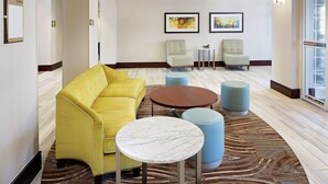 Un vestíbulo moderno con un sofá amarillo, una mesa de mármol y dos sillones.