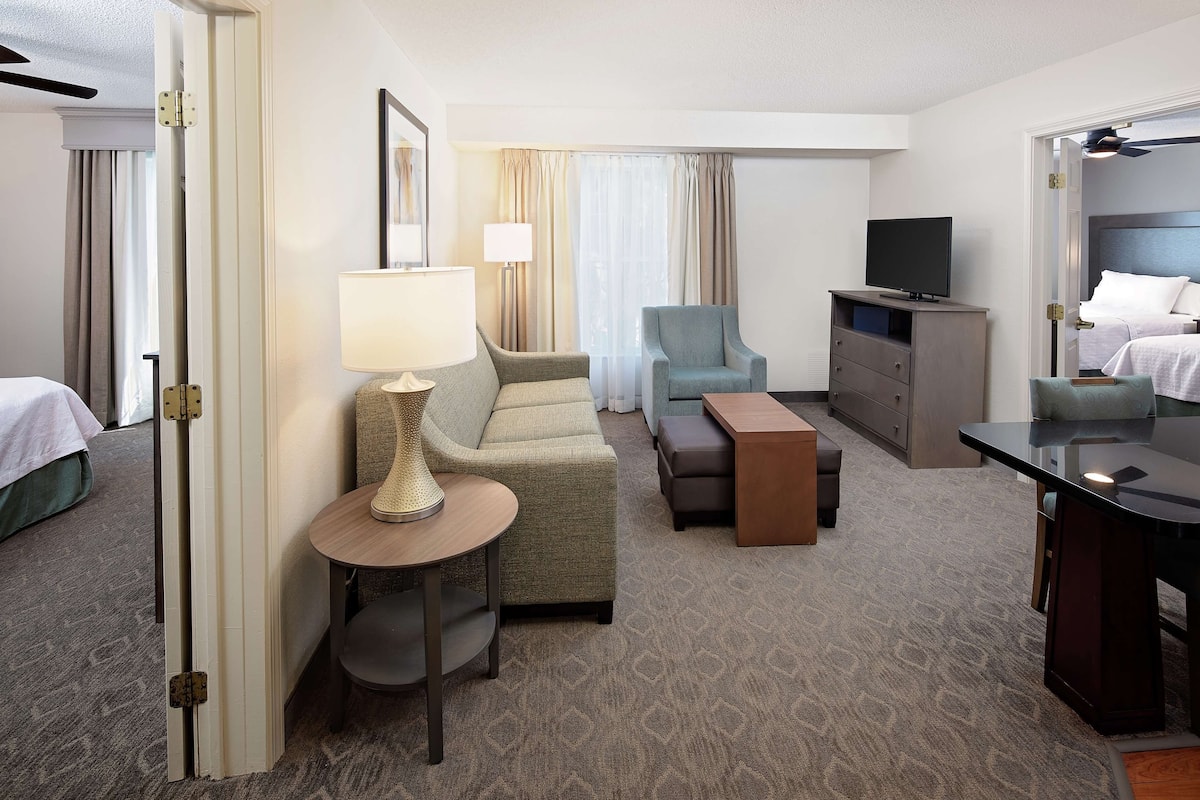Habitación de hotel con cama, sofá, escritorio, silla, televisor y lámpara.