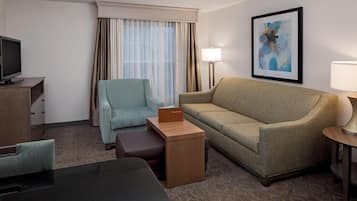 A hotel room with a sofa, armchair, a small table, a TV, and a painting on the wall.