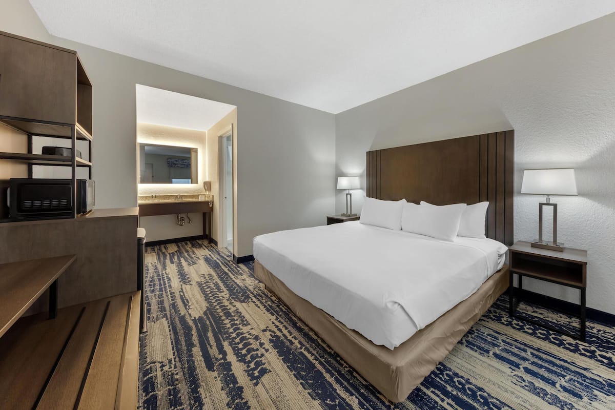 A hotel room with a large bed, bedside tables with lamps, a desk with a chair, and a patterned carpet.