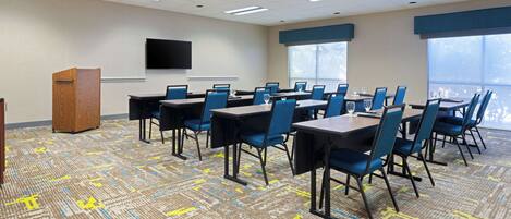 A conference room with multiple tables and chairs, a podium, and a large screen on the wall.
