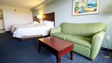 A hotel room with two beds, a green sofa, a wooden table, and a painting on the wall.