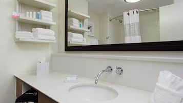 A bathroom with a white sink, a mirror, and shelves with towels and toiletries.