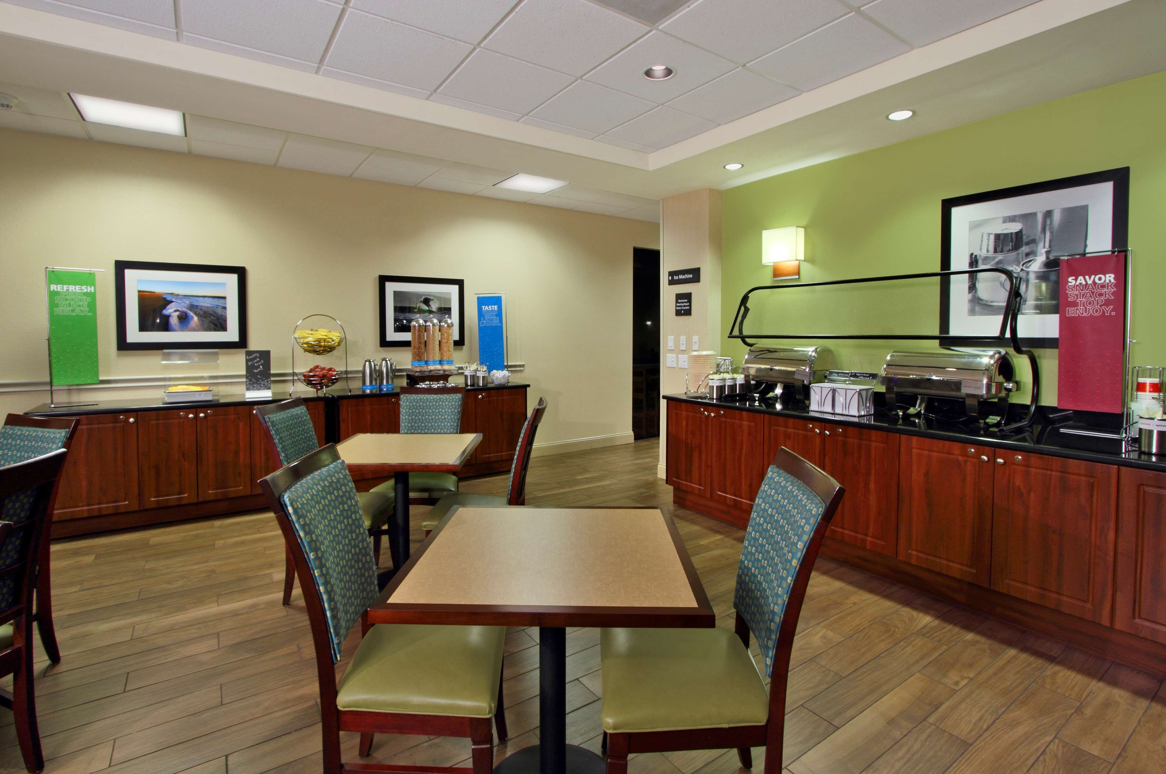 A hotel dining area with wooden tables and chairs, a buffet counter, and a green accent wall.