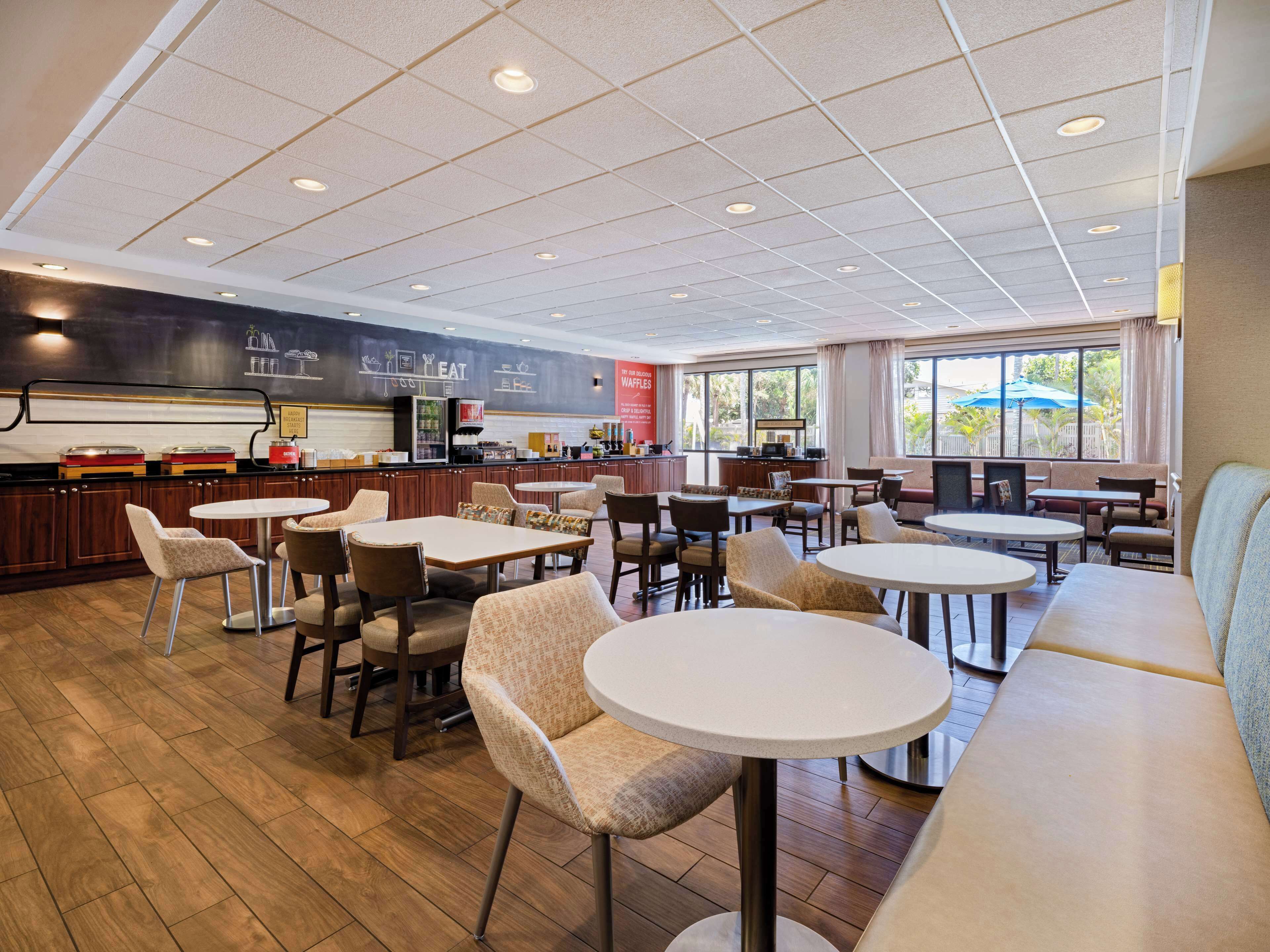 Een modern restaurant met verschillende zitmogelijkheden, zoals tafels en zitbanken, en een keuken in de achtergrond.