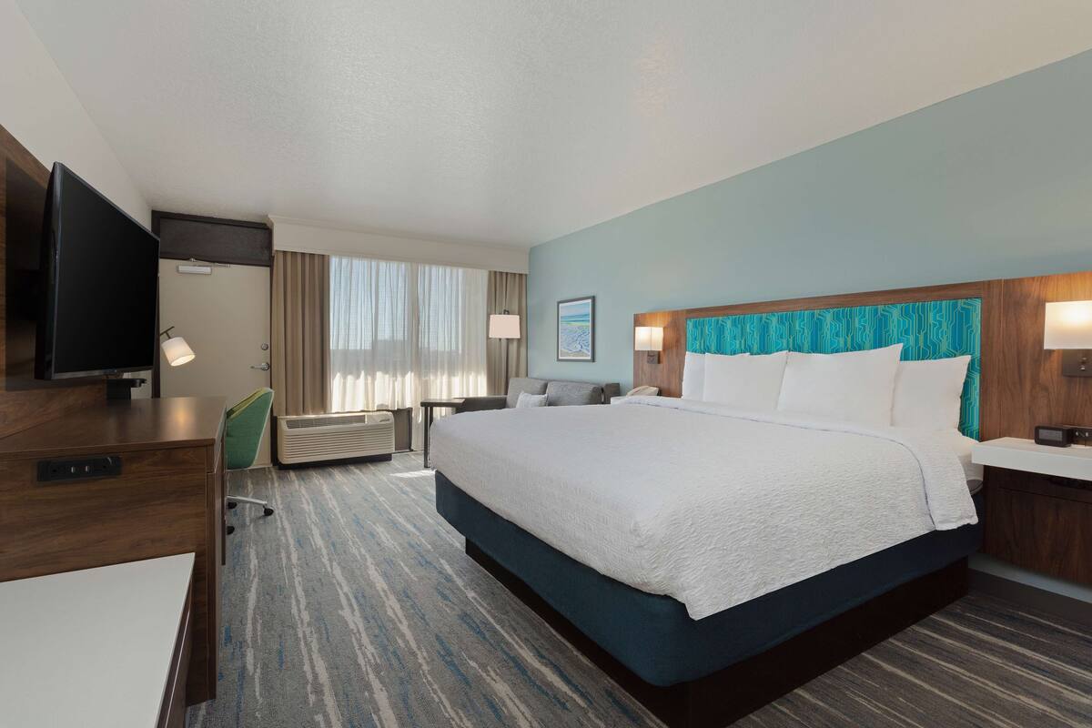 A hotel room with a large bed, a desk, a television, and a window with curtains.