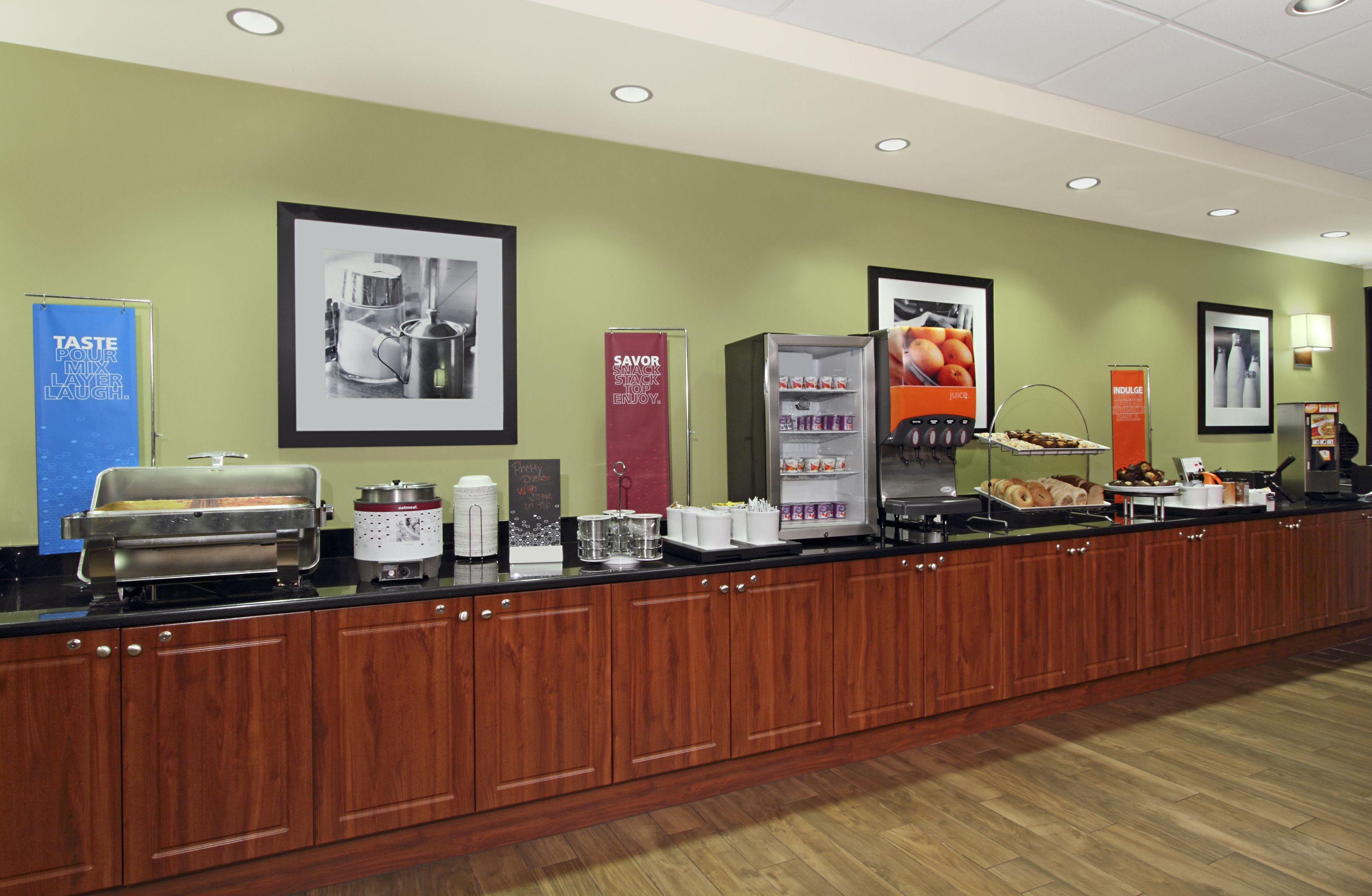 A buffet setup with various food items and beverages, including a coffee machine, a juice dispenser, and a refrigerator.